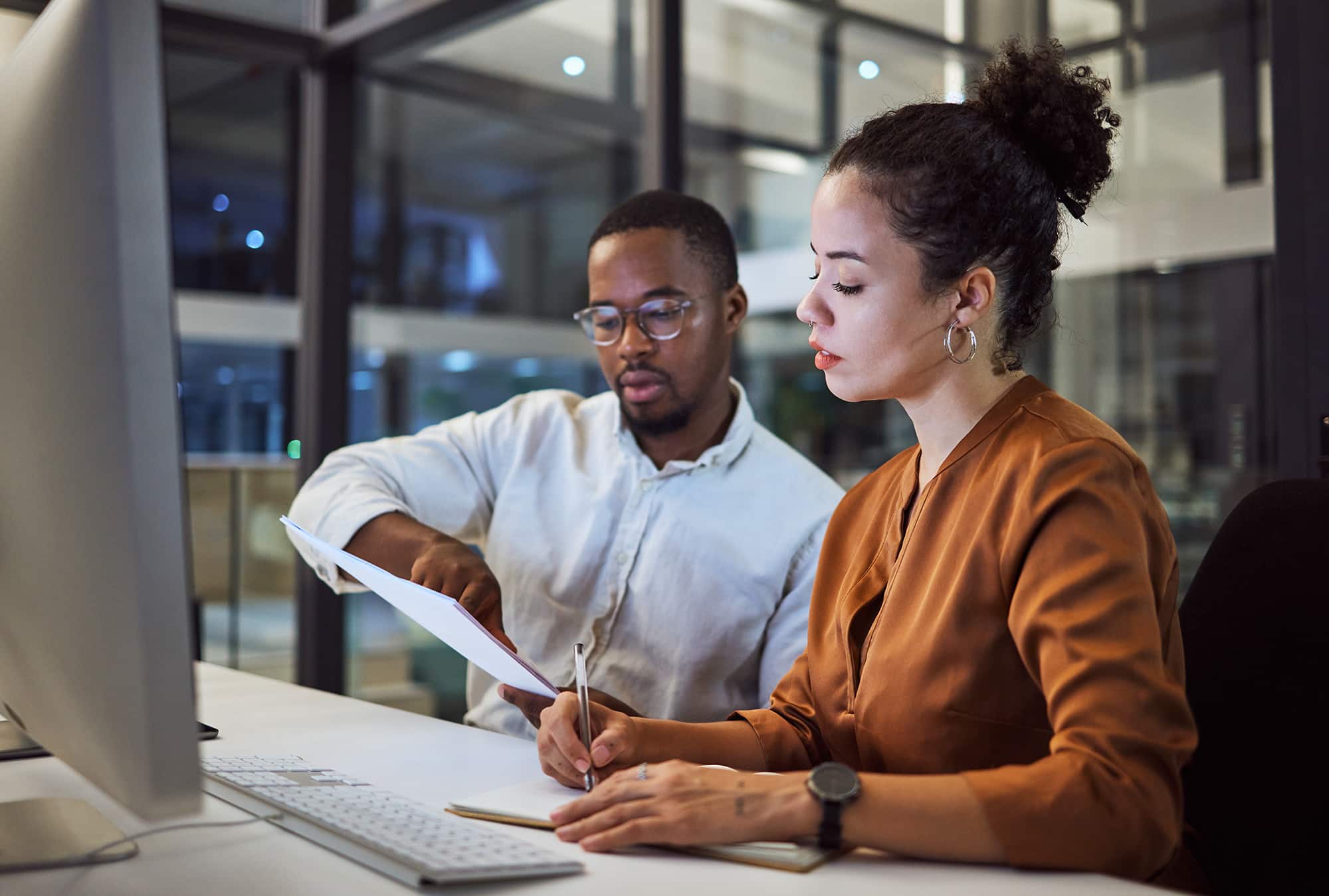 Teamwork in New York office at night, business document reading together and professional accounting report. Black man with financial audit, showing latino woman figures and employee collaboration.