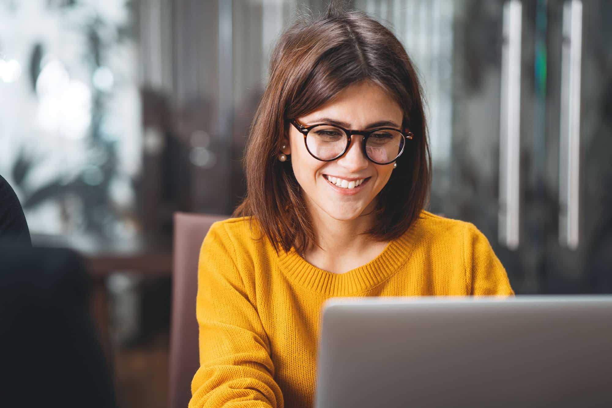 Portrait of happy business woman wearing glasses at workplace in office. Young handsome female worker using modern laptop