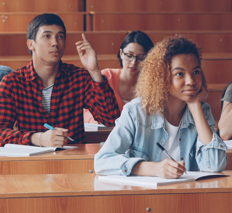 Multi-ethnic group of students is answering teacher's questions, smart young people are talking and smiling sitting in tables while teacher is asking them checking knowledge.