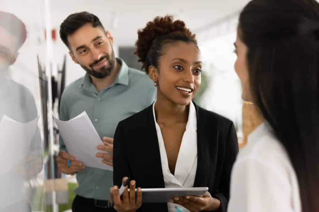 Smiling female business professional speak to teammates by planning board